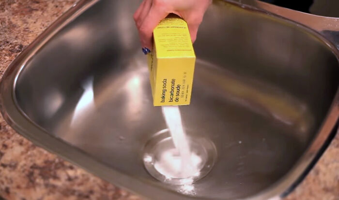 Person pouring baking soda into a kitchen sink as a life hack to clean or unclog it efficiently.