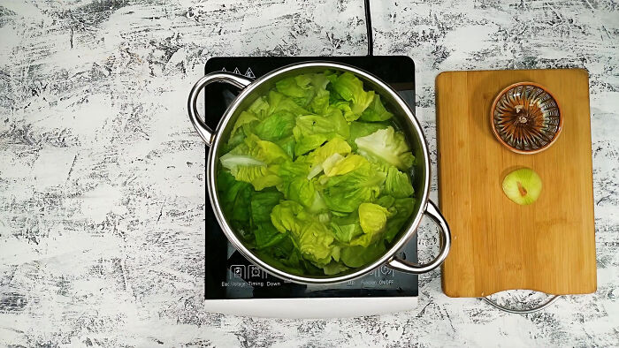 Cooking fresh lettuce in a pot on a stove next to a wooden cutting board with a juicer and apple slice.