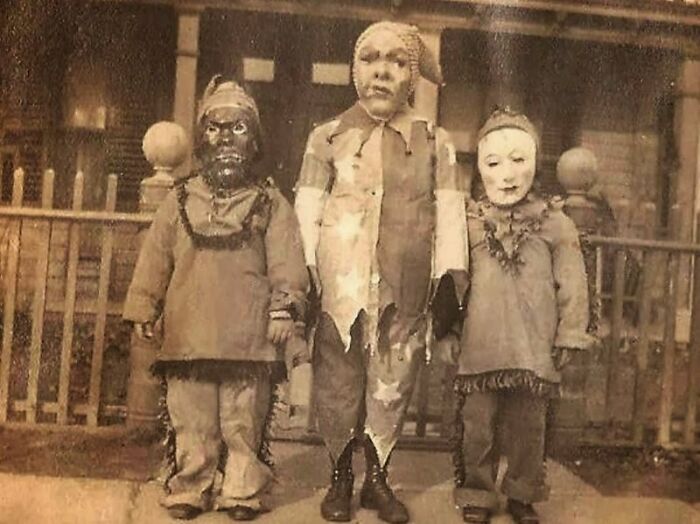 Three children in vintage Halloween costumes posing outside a house, showcasing early terrifying and impressive Halloween costumes.