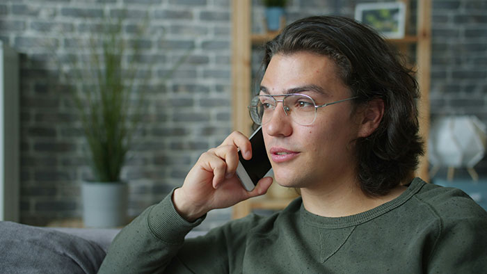 Young man with glasses making a phone call, reflecting on rejection and dating after being turned down thrice.