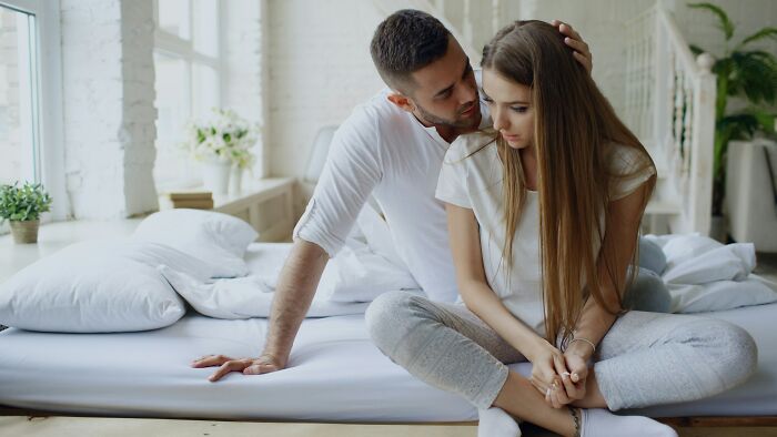 Couple sitting on bed in a bright room, sharing a quiet moment reflecting on relationship advice for stronger bonds.