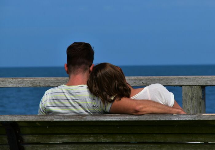 Couple sitting closely on a bench by the ocean, sharing a peaceful moment reflecting relationship advice and connection.