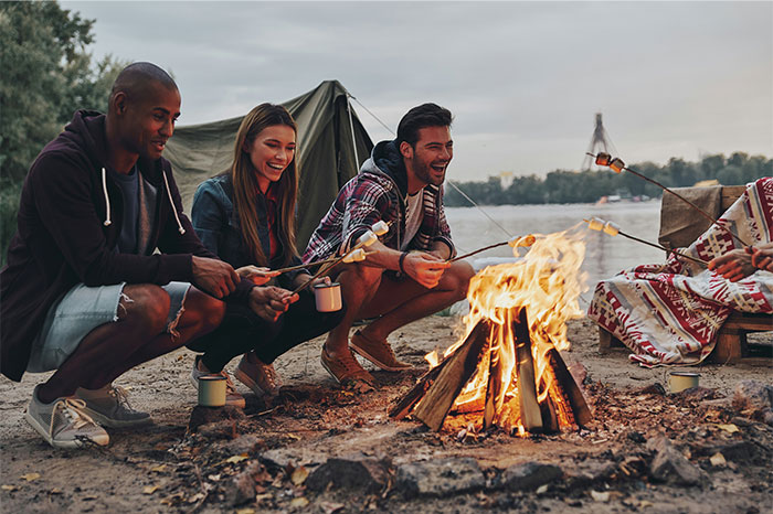 Three friends roasting marshmallows over a campfire by the lake, enjoying cooking smarter outdoors.