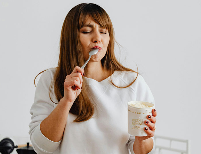 Woman tasting food with a spoon while holding a container, illustrating cooking smarter with kitchen cheats and blow dry chicken tips.