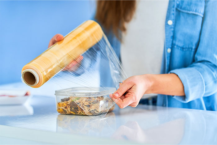 Person wrapping a container of cooked chicken with plastic wrap as a smart kitchen cooking cheat.