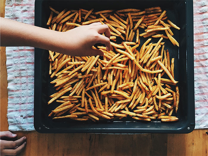 Hand reaching for crispy golden fries on a baking tray, illustrating cooking smarter kitchen hacks with easy meal prep.