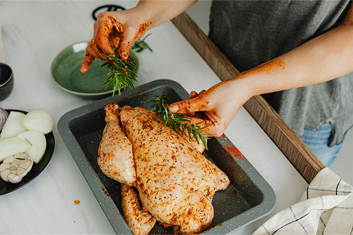 Person seasoning a whole chicken with herbs, demonstrating a smart cooking hack for preparing chicken easily.