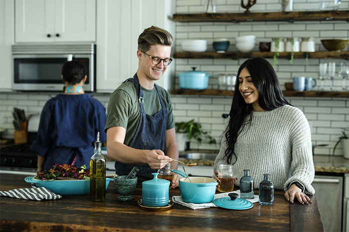 Three people in a modern kitchen using kitchen cheats to cook smarter with a blue pot and spices on the counter.