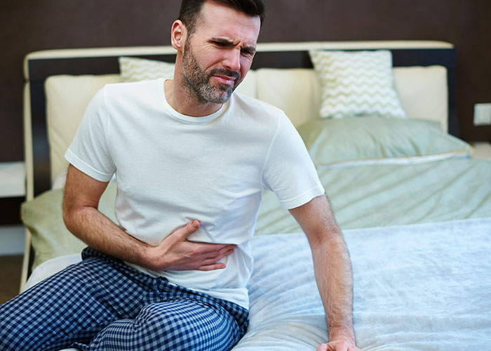 Hombre con dolor abdominal sentado en cama ilustrando síntomas relacionados con hallazgos sorprendentes en autopsias.