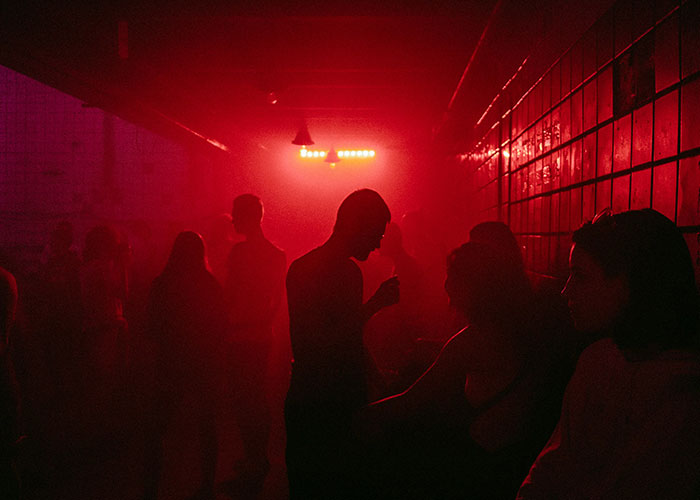 Personas en una habitación oscura con luz roja, ambiente dramático relacionado con hallazgos de médicos forenses.