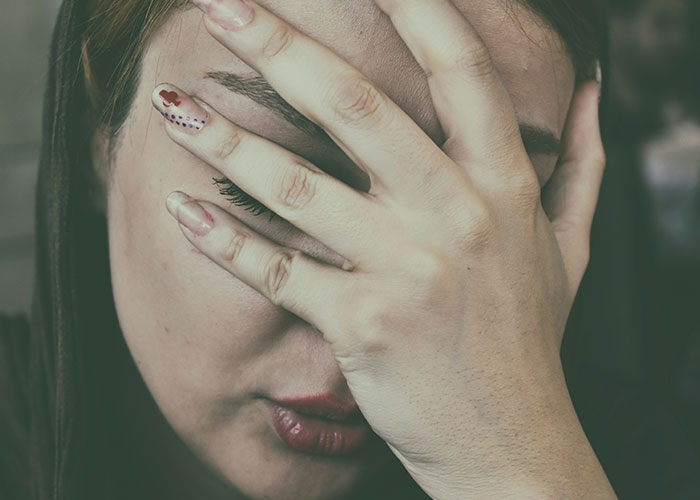 Mujer preocupada cubriéndose el rostro, ilustrando emociones ante hallazgos sorprendentes de médicos forenses en autopsias.