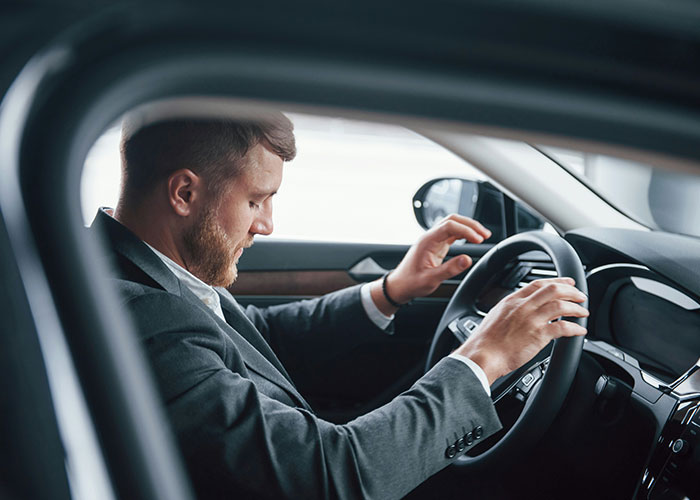 Hombre serio en traje sentado en auto, simbolizando sorprendentes hallazgos de médicos forenses durante autopsias.
