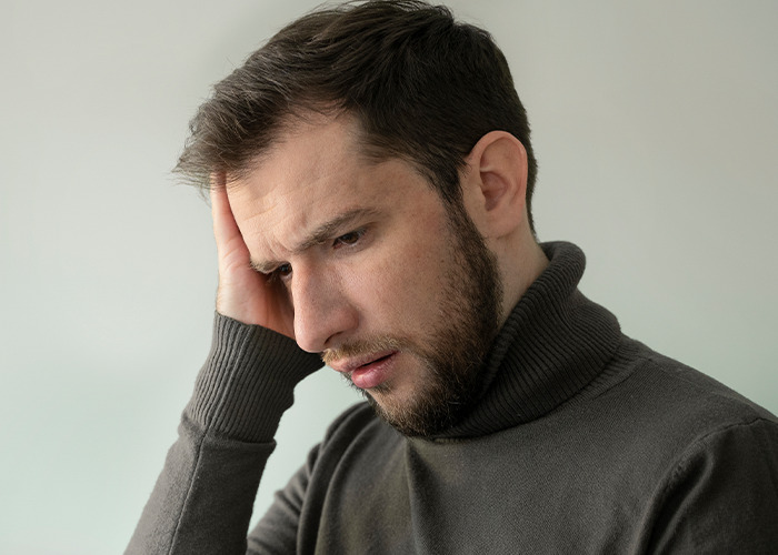 Worried man in a gray sweater holding his head reflecting on dad in maternity wards stories and challenges
