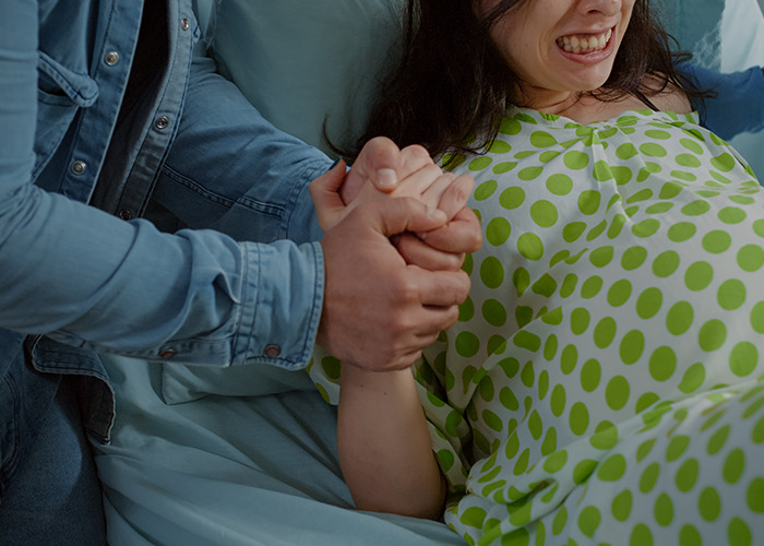 Pregnant woman in labor gripping partner's hands in maternity ward, capturing tense moments of dad in maternity wards stories.