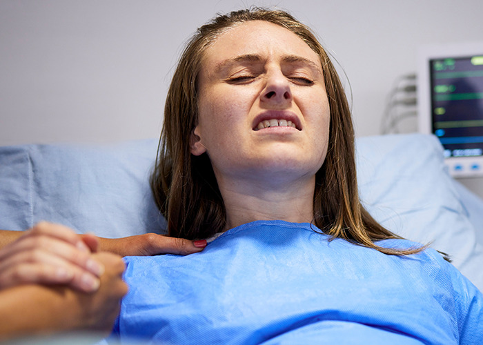 Woman in labor holding partner’s hand in a hospital bed, capturing raw emotion in a maternity ward setting.