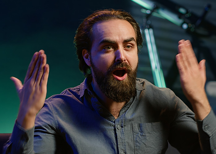 Bearded man with raised hands and surprised expression, sharing wild and infuriating dad in maternity wards stories.