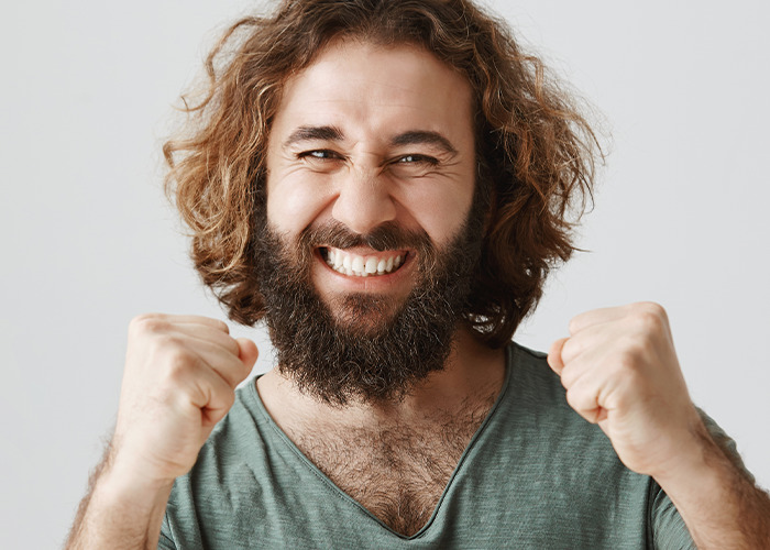 Bearded man celebrating with clenched fists, smiling widely, capturing the wild and infuriating dad in maternity wards moment.