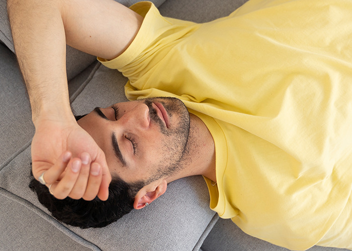 Man in a yellow shirt resting on a gray couch, illustrating a dad in maternity wards moment of exhaustion or relief.