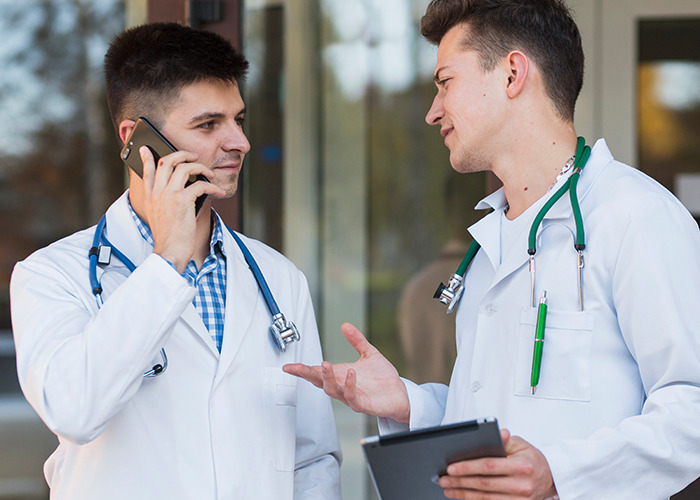Two male doctors talking outside hospital, one on phone, both wearing stethoscopes, related to dad in maternity wards stories.