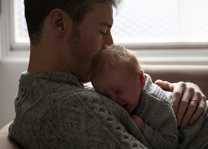 Man in maternity ward holding and comforting a crying baby, showcasing tender moments of dad and newborn bonding.