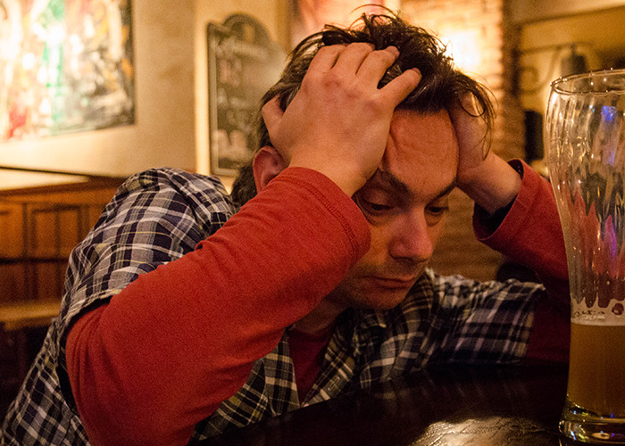 Stressed man in a plaid shirt sitting in a bar, capturing the frustration of dads in maternity wards stories.