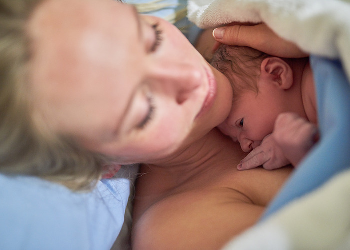 New mother holding newborn baby skin-to-skin in hospital room, capturing the raw emotions of maternity wards stories.
