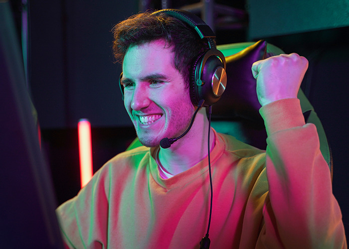 Young man wearing headphones with microphone, celebrating a win, shown in vibrant lighting, illustrating dad in maternity wards stories.