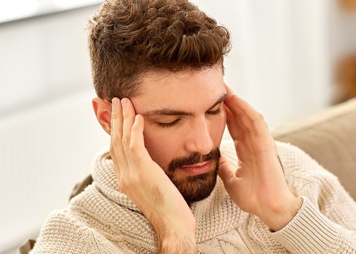 Young man in a cozy sweater holding his head, reflecting the stress of dad in maternity wards stories.