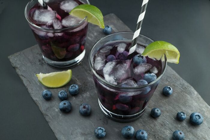 Two glasses of blueberry drink with ice and lime wedges on a dark slate board, representing strange health hacks.