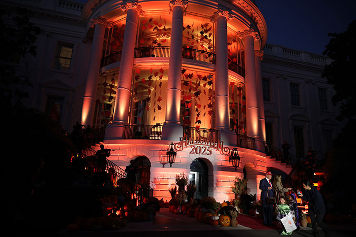 White House Halloween display illuminated with orange lights and autumn decorations during evening event in 2023.