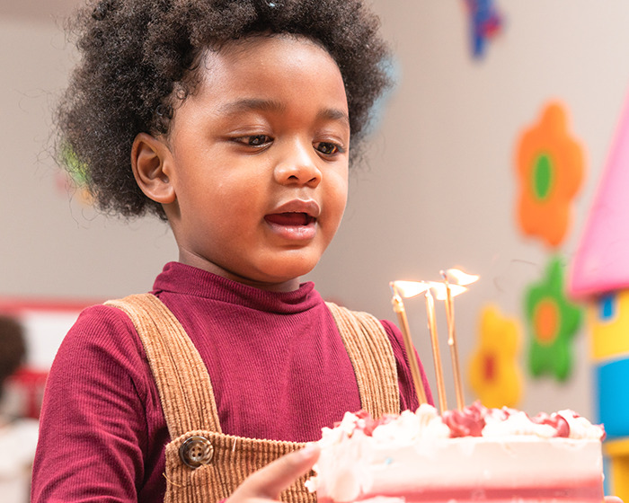 Young Black child celebrating birthday with cake and candles in colorful room related to teacher accused of racism case.