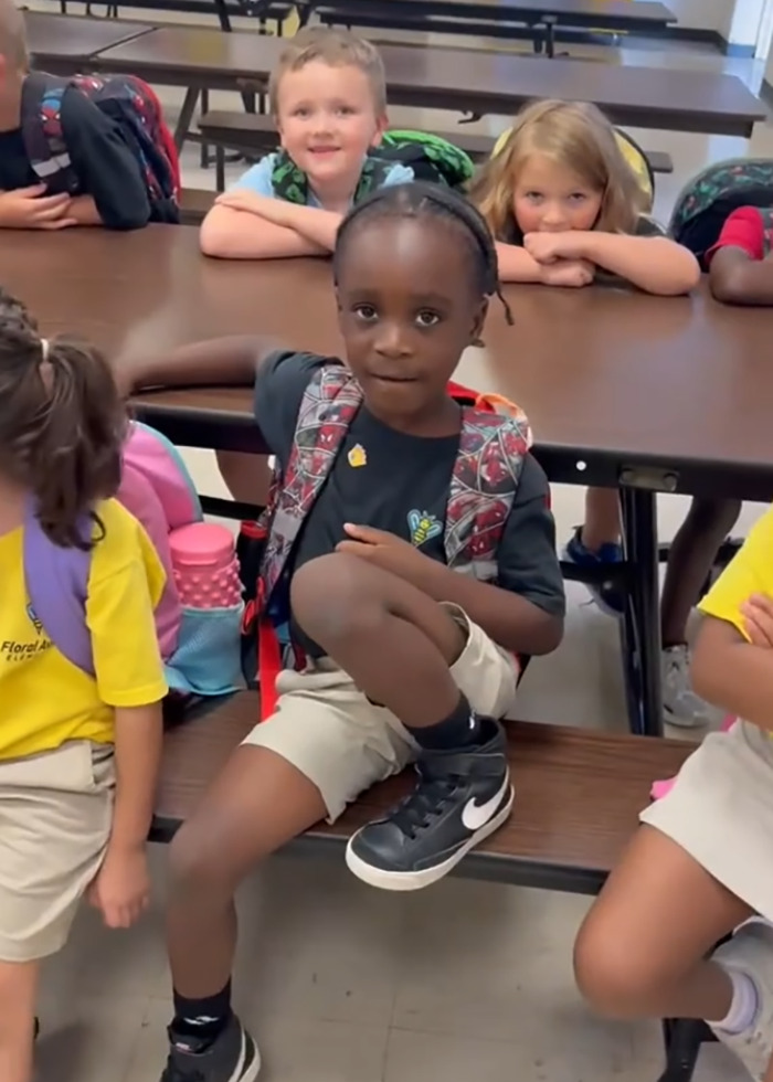 Black student sitting on a school bench surrounded by classmates, related to teacher accused of racism incident.