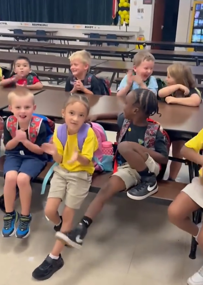 Group of young students sitting and clapping in a school cafeteria, illustrating teacher accused of racism incident.