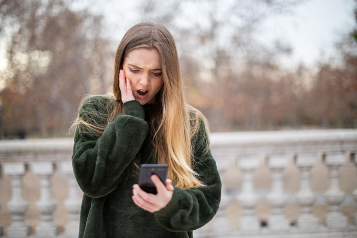 Young woman looking shocked and upset while reading on her smartphone outdoors, reflecting daughter calling husband a cheater.