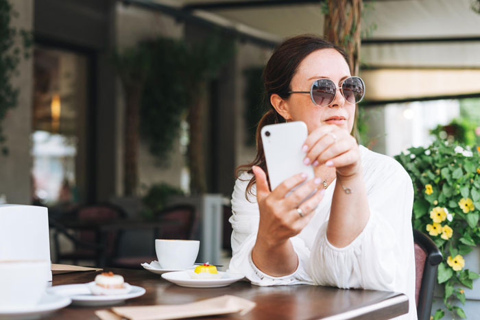 Woman in sunglasses holding a phone at a cafe, relating to wife taking free pass with John Krasinski topic.