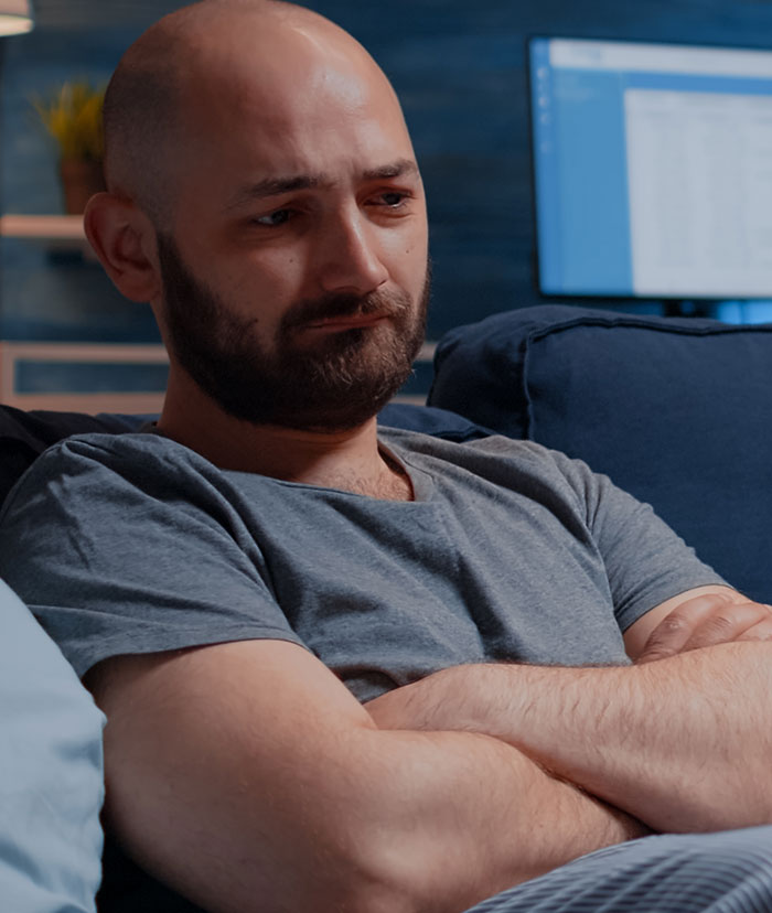 Man sitting on couch with arms crossed, looking upset and reflecting on missed hospital calls after an argument with wife.