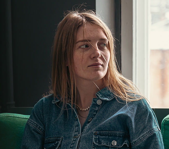 Woman looking upset and distracted while sitting indoors near a window, reflecting anger and concern after argument.