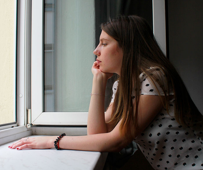 Woman looking out the window, upset and contemplative, reflecting the emotion of missing calls from the hospital after an argument.