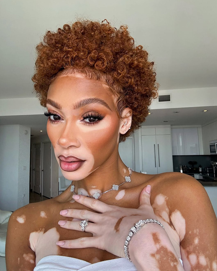 Winnie Harlow close-up portrait with curly hair and makeup, facing backlash after channeling Whitney Houston for Halloween.
