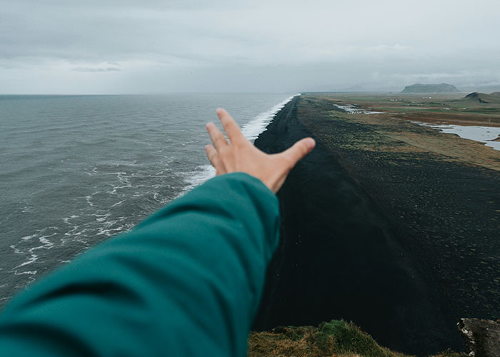 Person in a teal jacket reaching toward the ocean and black sand beach, illustrating instant karma manifestations.