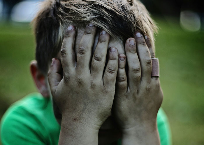 Young boy with dirty hands covering his face outdoors, illustrating a moment of instant karma manifestations.