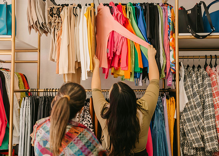 Two women browsing colorful clothing racks in a store, showcasing instant karma manifestations in daily life.