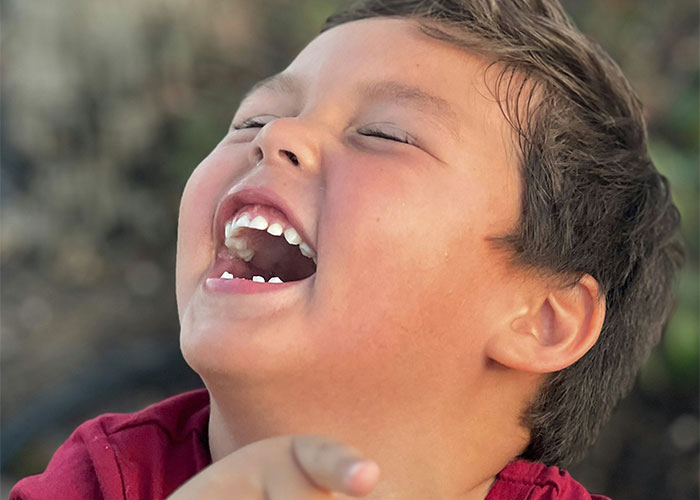 Young boy laughing joyfully outdoors, capturing a moment of happiness related to instant karma manifestations.