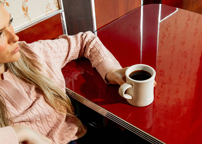 Woman in a pink sweater holding a white coffee cup, reflecting calm moments of instant karma manifestations.