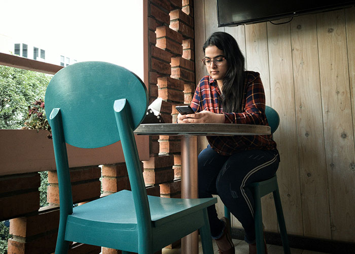 Young woman sitting at a rustic café table using her phone, illustrating people sharing instant karma manifestations.