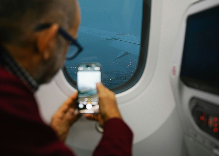 Man taking a photo of airplane wing through window, capturing a moment of instant karma manifestation in flight.