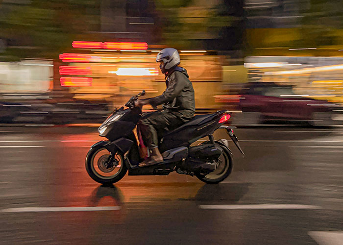 Person riding a motorbike at night with blurred city lights capturing instant karma manifestations in motion.