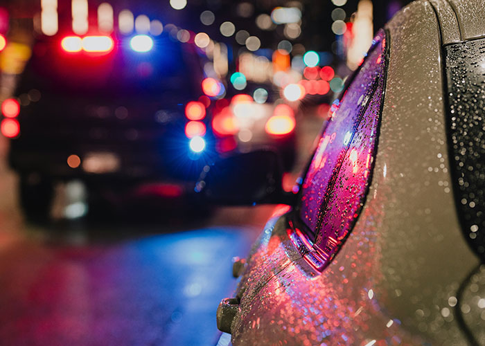 Police car with flashing lights behind a raindrop-covered vehicle, illustrating instant karma manifestations in traffic situations.