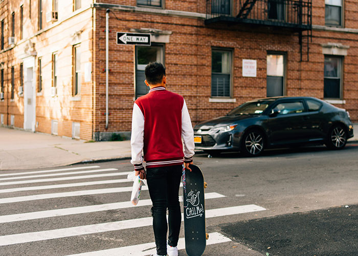 Young person holding a skateboard and walking on a city street, capturing an instant karma manifestation moment.
