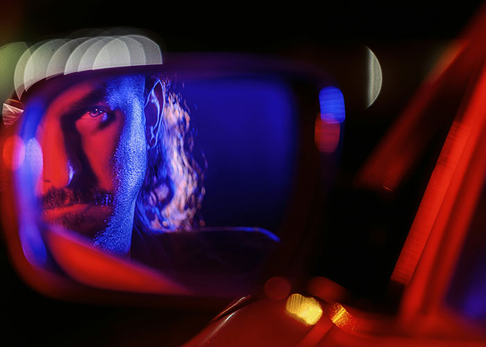 Man's intense face reflected in a car side mirror with dramatic red and blue lighting, capturing instant karma concept.